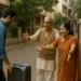 A young Indian man returns home with a suitcase as his elderly parents welcome him warmly outside their house in a quiet residential lane.