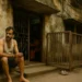 A weary middle-aged Indian man sits outside a rundown two-storey house in Virar, as his wife teaches tuition inside