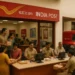 A busy India Post office with customers, computers, and red delivery vehicles showing modernization in the 2000s.